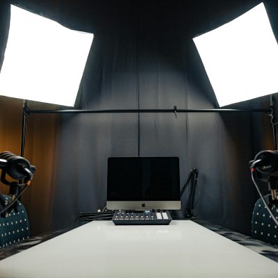 A modern podcast recording studio with microphones, lighting, and computer equipment.