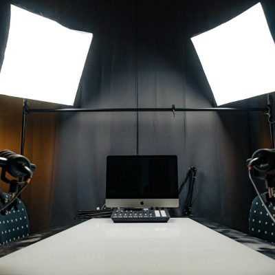 A modern podcast recording studio with microphones, lighting, and computer equipment.