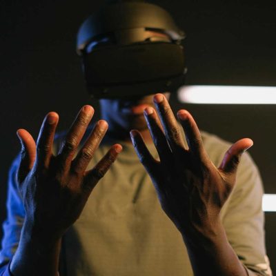 Black man using VR goggles with outstretched hands in a tech environment.