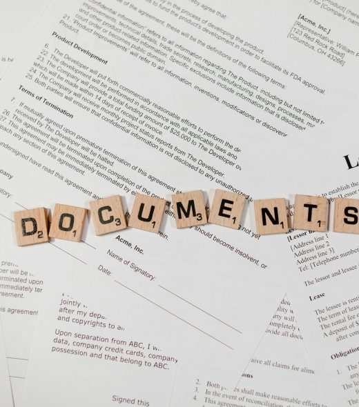 Top view of scrabble tiles spelling 'DOCUMENTS' on various contracts and agreements.