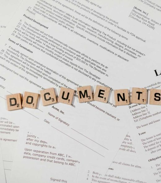 Top view of scrabble tiles spelling 'DOCUMENTS' on various contracts and agreements.