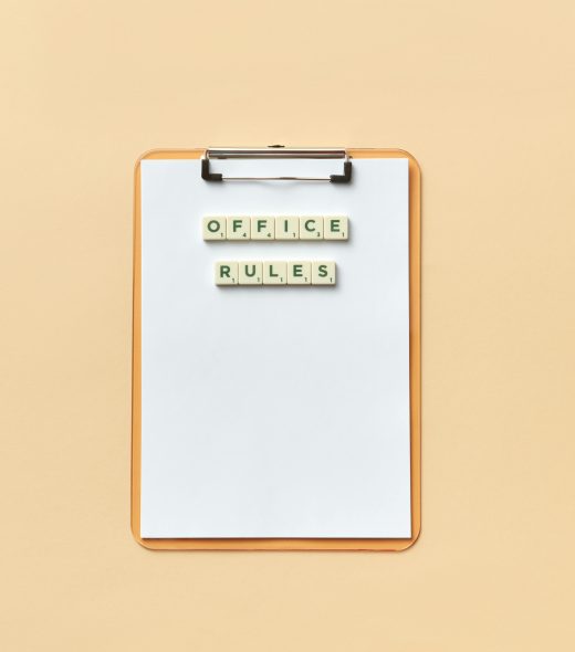 A clipboard with the phrase 'Office Rules' spelled out using Scrabble tiles on a beige background.