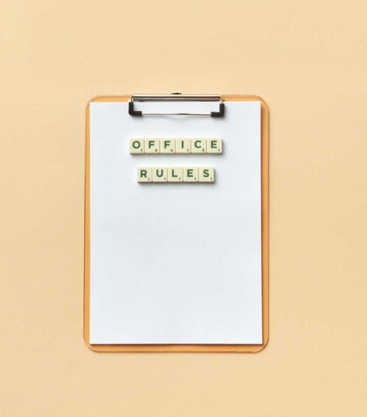A clipboard with the phrase 'Office Rules' spelled out using Scrabble tiles on a beige background.
