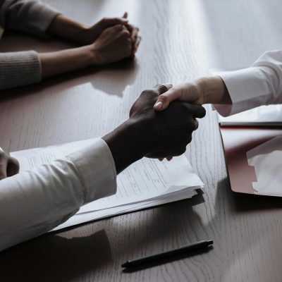 Business agreement with a handshake over contract documents at a meeting table.