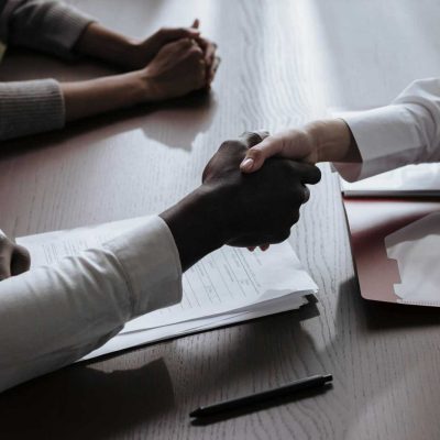 Business agreement with a handshake over contract documents at a meeting table.